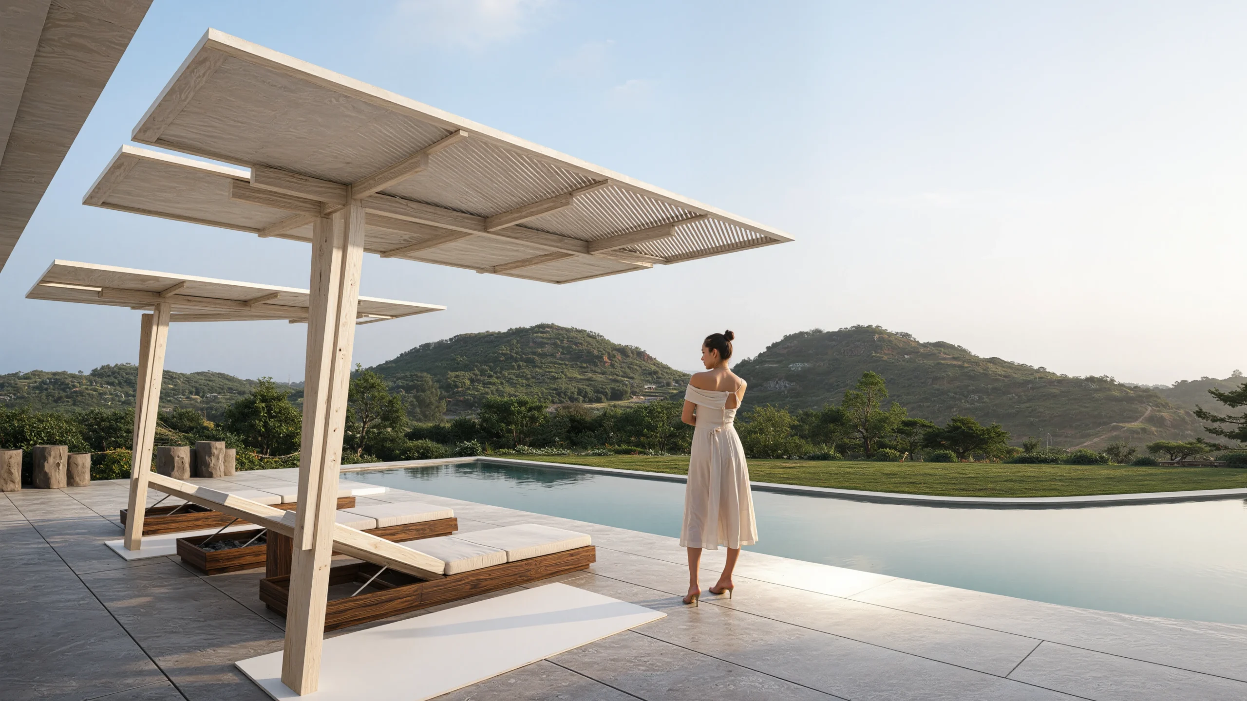 Woman in an off‑the‑shoulder beige dress standing by an infinity pool under a large wooden pergola with hills in the background.