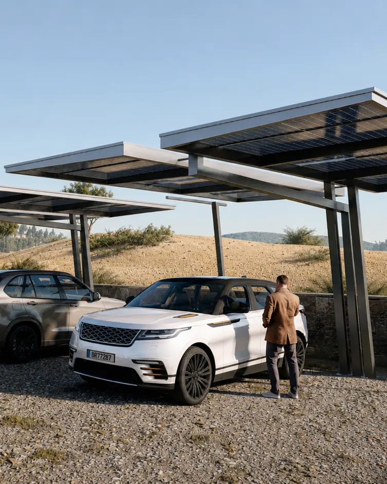 Man in a brown jacket stands beside a white SUV parked under solar-panel carport in a desert lot.